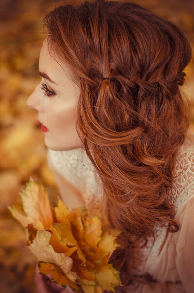 Portrait of a beautiful young girl with and braided hair and a bouquet of autumn leaves in the hands, a gentle long dress