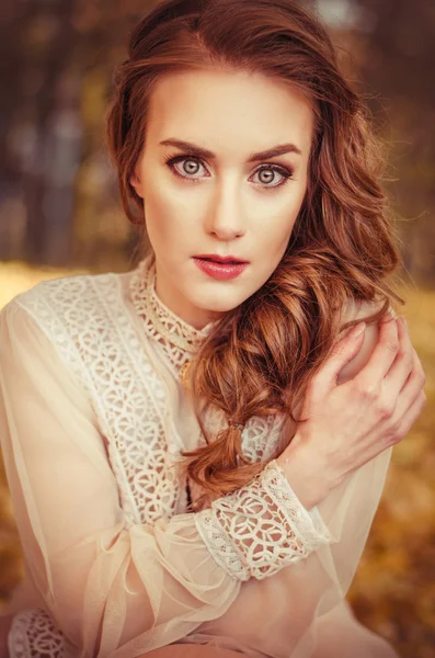 Retrato de una hermosa joven con ojos azules, un suave vestido de melocotón sobre un fondo de hojas de otoño — Foto de Stock