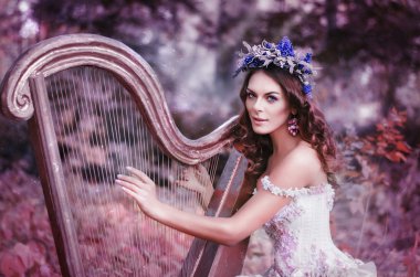 beautiful brown-haired woman with a flower wreath on her head, wearing a white dress playing the harp in the forest