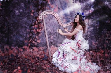 beautiful brown-haired woman with a flower wreath on her head, wearing a white dress playing the harp in the forest