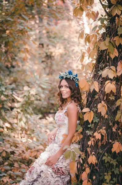 Beautiful brown-haired woman in a long white dress, with a wreath of lavender on her head, is in the fairy forest — 图库照片