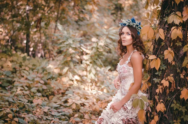 Beautiful brown-haired woman in a long white dress, with a wreath of lavender on her head, is in the fairy forest — Stock Photo, Image