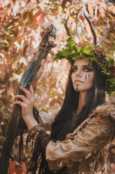 Retrato de una morena con cara pintada en la imagen de chamán y corona floral en la cabeza y cuernos —  Fotos de Stock