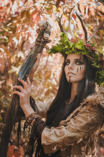 Portrait of a brunette with a painted face in the image of shaman and floral wreath on her head and horns