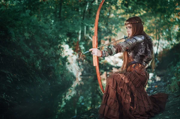 Mulher caçadora com um arco na mão, apontando para sua presa na floresta. Amazonas com um arco nas mãos da floresta . — Fotografia de Stock