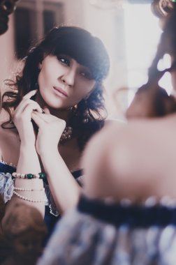 portrait of a beautiful brunette in a blue historic, vintage dress of the 19th century, looking at himself in the mirror