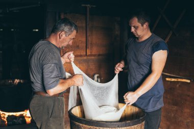 Karpat Dağları, Ukrayna - Ağustos 2020: Çiftlik peyniri yapan iki adam. Peynir bezinden süt süzülüyor..