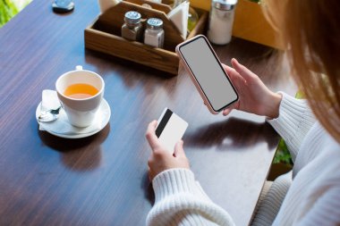 Bir kafede cep telefonuyla kart ödemesi yapan bir kadının yakın görüntüsü..