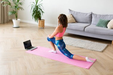 Evde dizüstü bilgisayarın önünde gerinen bir kadın..