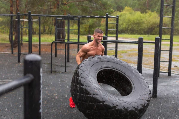 Mann kippt einen Reifen um. Outdoor-Workout an einem regnerischen Tag. — Stockfoto