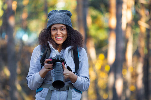 Улыбающаяся афроамериканка в лесу с камерой.