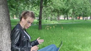 Dizüstü bilgisayarı ve kulaklığı olan genç bir kadın kampüs parkında otururken internette sohbet ediyor..