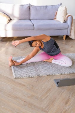 Afro-Amerikalı bir kadın evinde dizüstü bilgisayar ekranının önünde geriliyor..