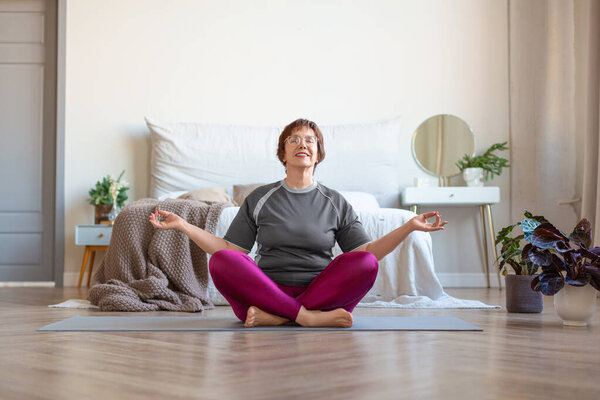 Senior woman meditates at home in the lotus position. Healthy lifestyle concept.