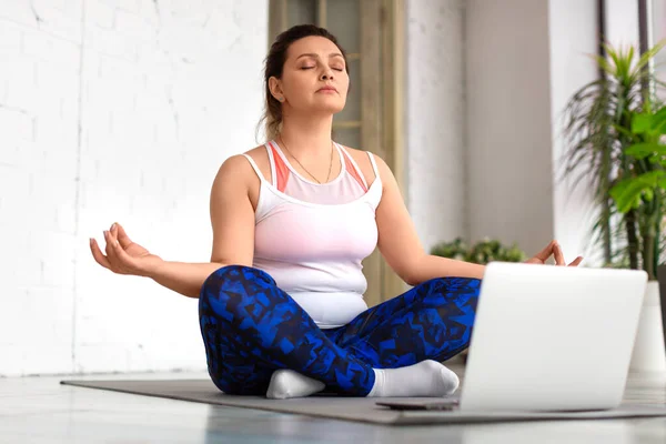 Gözleri kapalı bir kadın iç mekanda dizüstü bilgisayarın önünde meditasyon yapıyor. Sağlıklı yaşam tarzı kavramı. — Stok fotoğraf