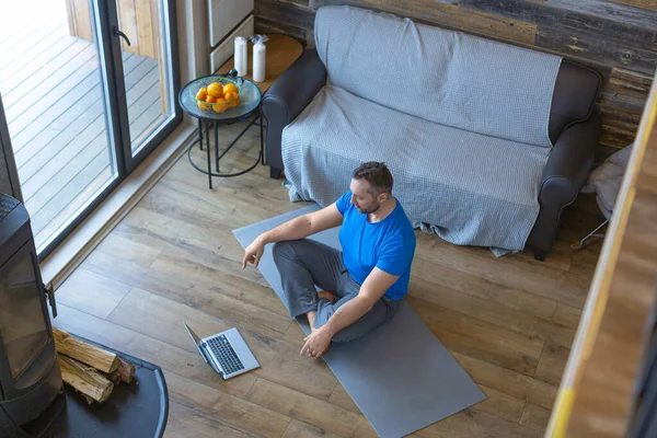 Relaxation and mental health. Man meditates at home in front of a laptop. Onein yoga tutorial.