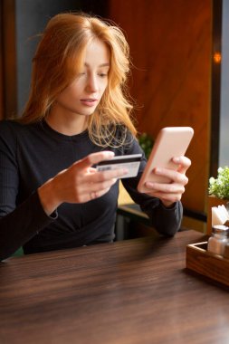Faturaları ödemek için cep telefonuyla kart ödemesi yapan bir kadın. Dikey fotoğraf.