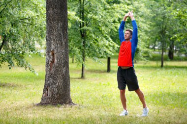 Kaslarını esneten bir adamın fotoğrafı. Spor ve sağlıklı yaşam tarzı konsepti. Şehir parkında egzersiz..