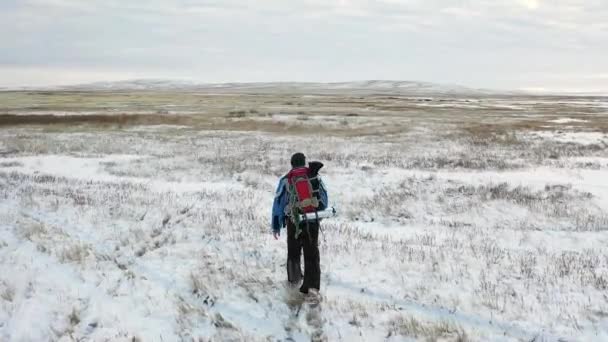 En ensam vandrare går över ett oändligt snöfält. Resekoncept i extrema förhållanden. Utsikt bakifrån. — Stockvideo