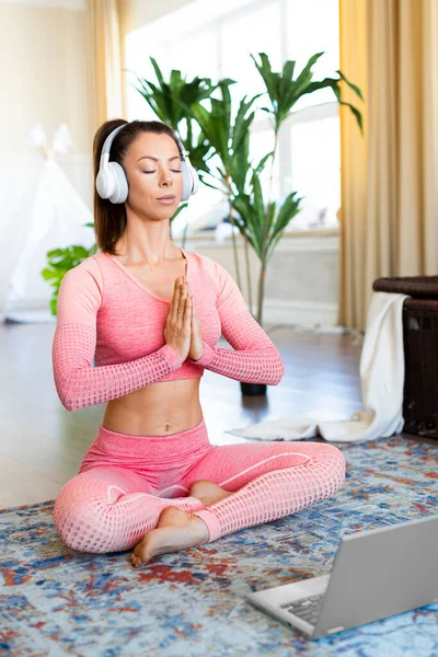 Verticale foto. Meditatie praktijk - jonge vrouw in witte hoofdtelefoon tijdens online yoga praktijk. — Stockfoto