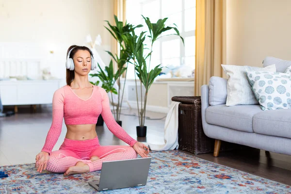 Evde meditasyon uygulaması - çevrimiçi yoga dersi sırasında beyaz kulaklıklı genç bir kadın. — Stok fotoğraf
