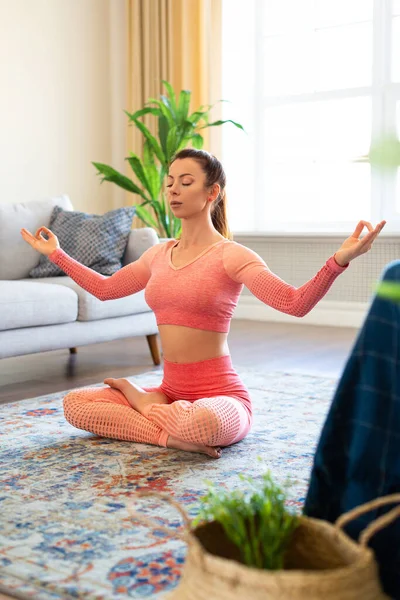 Kadın evde meditasyon yapıyor. Gözleri kapalı lotus pozisyonunda oturuyor ve yoga meditasyonu yapıyor. Dikey fotoğraf. — Stok fotoğraf