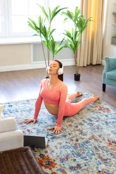 Жінка виконує вправи з кобри перед монітором ноутбука. Онлайн заняття з йоги під час карантину. Вертикальне фото . — стокове фото