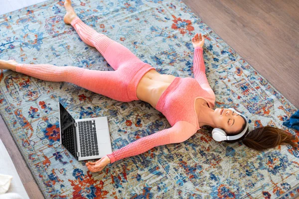 İnternetteki yoga dersinde gözleri kapalı yatan bir kadın. Sakinleştirici müzikle antrenmandan sonra dinlenme.