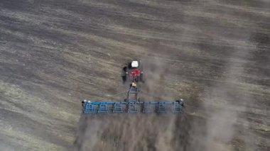 Kırmızı traktör, güneşli bahar havasında kahverengi toprağı işliyor. Hava görünümü.