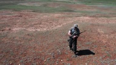 Yaralı ve yorgun bir keskin nişancı askeri sıcak çöl zemininde yürüyor. Olağanüstü koşullarda askeri çatışma ve hayatta kalma kavramı.