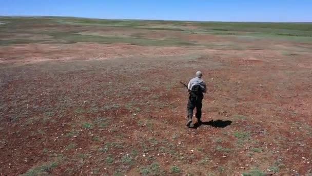 Soldado-atirador cansado caminha através da terra do deserto escaldante. Vista de trás. — Vídeo de Stock