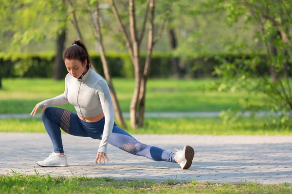 Pełnowymiarowe zdjęcie kobiety podczas treningu na świeżym powietrzu. Rozciąga mięśnie nóg i ogrzewa się przed treningiem joggingowym. — Zdjęcie stockowe