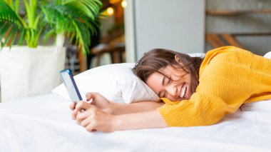Yatakta telefonu olan mutlu bir kadın. Mutlu bir şekilde gülüyor.