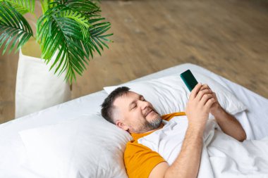 Uyandıktan sonra mesajlarını akıllı telefondan kontrol eden orta yaşlı bir adam..