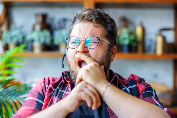 A young man in front of a webcam during an online video call. He yawns and covers his mouth with his hand. — Stock Photo, Image