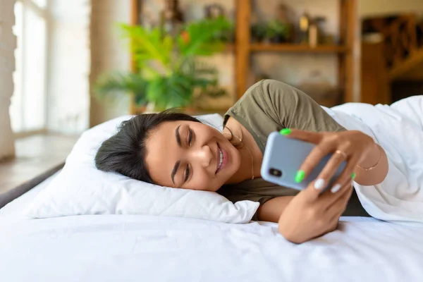 Une femme asiatique est couchée avec un téléphone portable. Elle s'est réveillée et vérifiait les messages sur les réseaux sociaux. — Photo