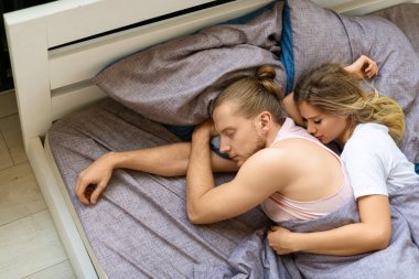 Sevgi dolu çift yatakta uyuyor. Kadın kocasına arkadan sarılıyor. İyileşme ve sağlıklı uyku konsepti.