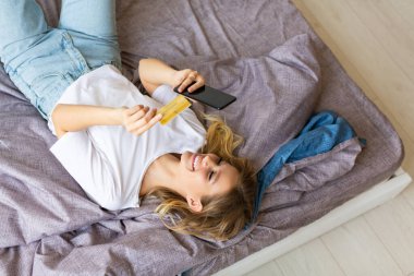 Yatakta yatan bir kadın mobil bir uygulama aracılığıyla sipariş veriyor. Çevrimiçi alımlar için kart numarasını çeviriyor..