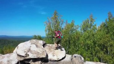 Sırt çantalı bir adam fotoğraf çekmek için dağın tepesine tırmanır. Kamera turisti takip ediyor..