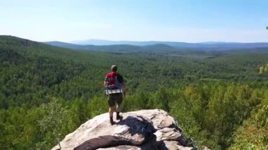 Bir turist fotoğrafçı fotoğraf çekmek için dağın tepesine tırmandı. Duruyor ve manzaranın tadını çıkarıyor. Kamera turistin etrafında uçuyor..