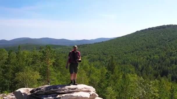 Bir turist fotoğrafçı dağın tepesinde duruyor ve manzaranın tadını çıkarıyor. Kamera turistin etrafında uçuyor.. — Stok video