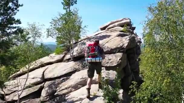Un homme avec un sac à dos monte au sommet de la montagne pour prendre une photo. L'unité avec la nature et le concept d'un mode de vie actif. La caméra suit le touriste. — Video