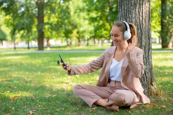 Jeune femme avec smartphone dans le parc de la ville lors d'un appel vidéo en ligne. Concept de travail en ligne ou concept d'enseignement en ligne à distance. — Photo