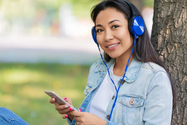 Portrait rapproché de femme asiatique dans des écouteurs avec smartphone. Elle sourit et écoute sa musique préférée ou sa leçon éducative. — Photo