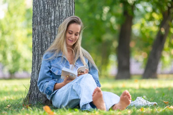 Poziome zdjęcie kobiety z książką w parku. Siedzi na trawie w parku i czyta bajki. Koncepcja odpoczynku od gadżetów, smartfonów i Internetu. — Zdjęcie stockowe
