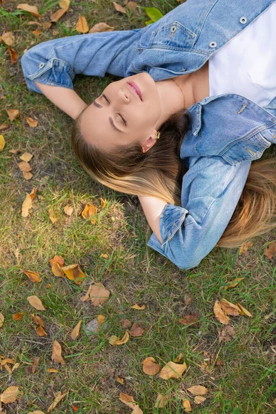 Conceito de desintoxicação digital - jovem mulher pensativa encontra-se no parque na grama com os olhos fechados. — Fotografia de Stock