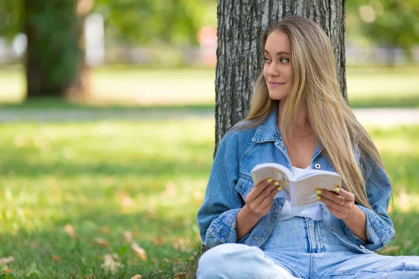Portret kobiety czytającej książkę siedzącej w parku na trawie. Koncepcja odpoczynku od gadżetów i zgiełku miasta. — Zdjęcie stockowe