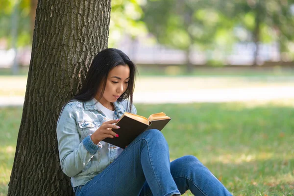 Azjatka z książką pod drzewem w parku. Koncepcja detoksykacji cyfrowej. — Zdjęcie stockowe