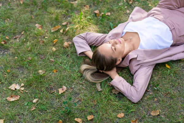 Conceito de desintoxicação digital - jovem mulher pensativa encontra-se no parque na grama com os olhos fechados. Vista superior de close-up. — Fotografia de Stock