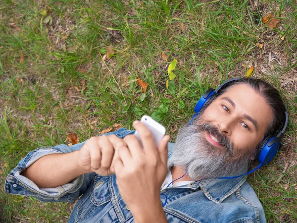 Orta yaşlı bir adamın şehir parkında çimlerin üzerinde yatarken müziğin tadını çıkarmasının en iyi görüntüsü.. — Stok fotoğraf